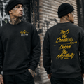 Person wearing a black sweatshirt with yellow text, standing against a textured wall.